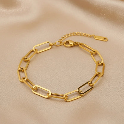 Gold paperclip chain bracelet laid flat on champagne satin fabric, highlighting its modern rectangular links and warm glow | Oria Jewel
