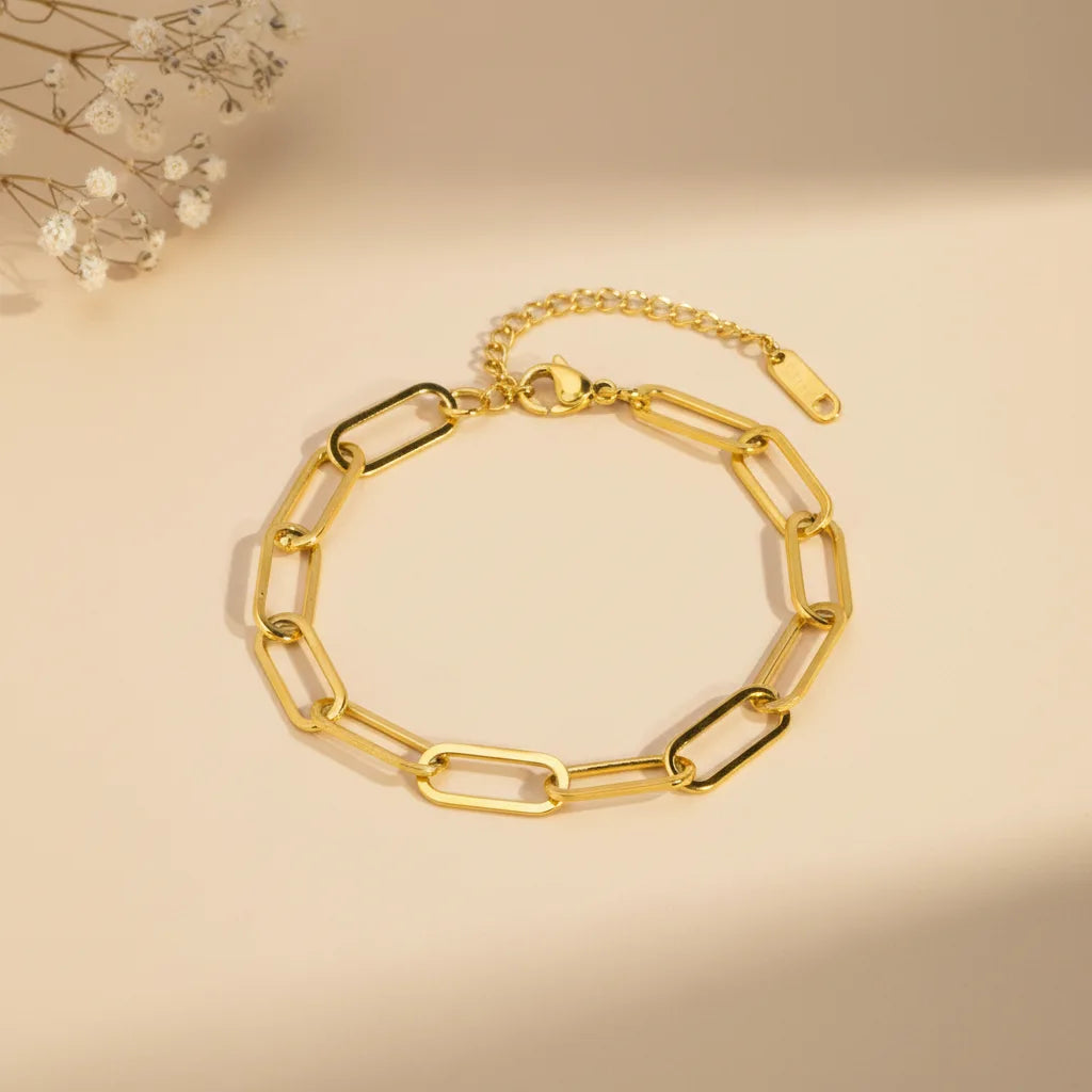 Gold paperclip chain bracelet arranged in a circle on a warm beige backdrop with delicate dried flowers in the corner | Oria Jewel