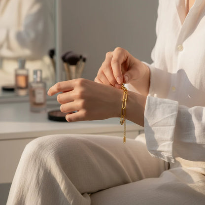 Close-up of a woman fastening her gold paperclip chain bracelet at a vanity, surrounded by soft morning light | Oria Jewel