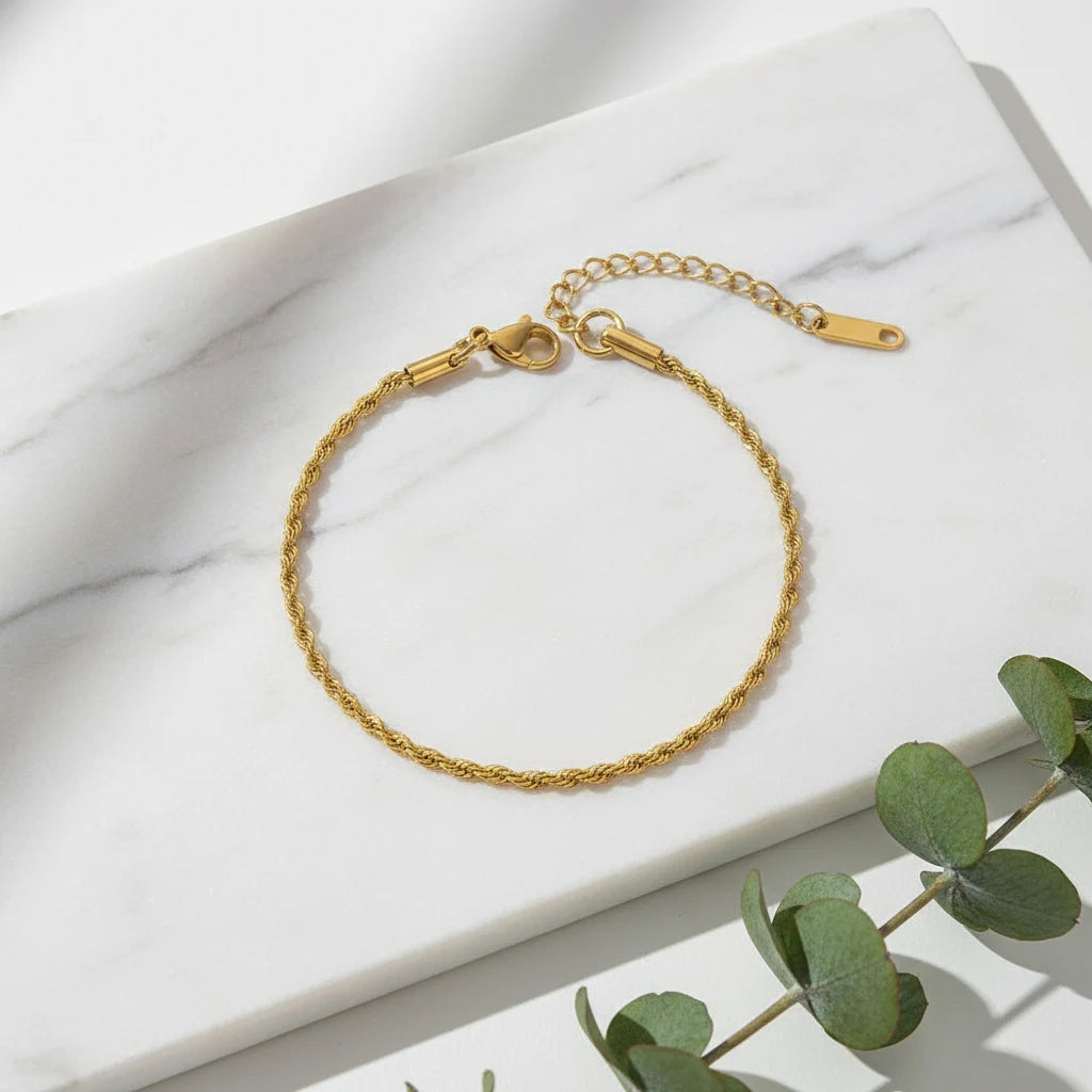 Gold rope chain bracelet laid in a neat circle on a white marble slab with green eucalyptus leaves adding a fresh natural touch | Oria Jewel
