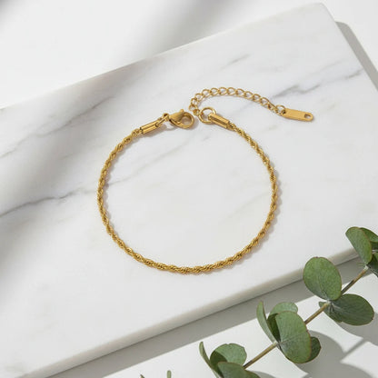 Gold rope chain bracelet laid in a neat circle on a white marble slab with green eucalyptus leaves adding a fresh natural touch | Oria Jewel