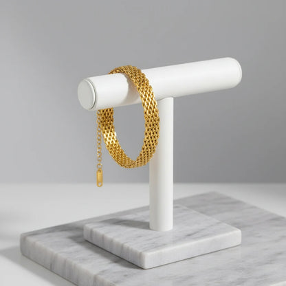 Gold wheat chain bracelet draped around a white jewelry stand on marble display surface | Oria Jewel