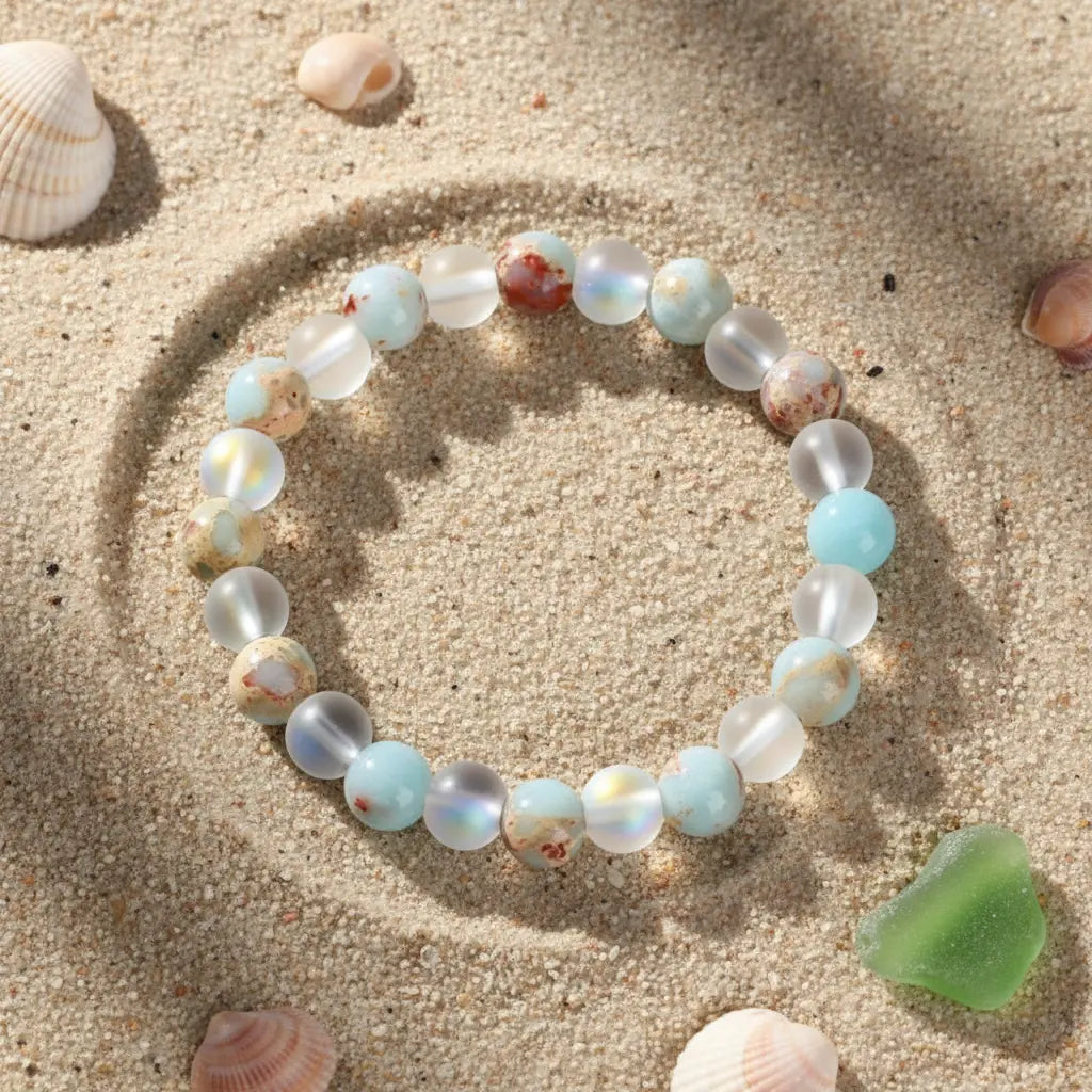 Luck &amp; Health Stone Bracelet arranged on sunlit beach sand with seashells and green sea glass, evoking a relaxed coastal energy vibe | Oria Jewel