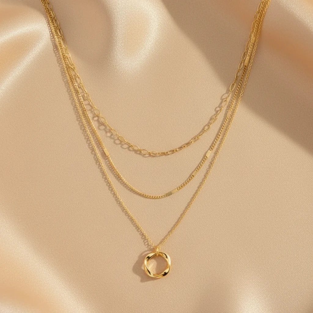 Close-up of Multi Layered Gold Chain Necklace on soft satin fabric — 18K gold shine with twisted pendant detail | Oria Jewel