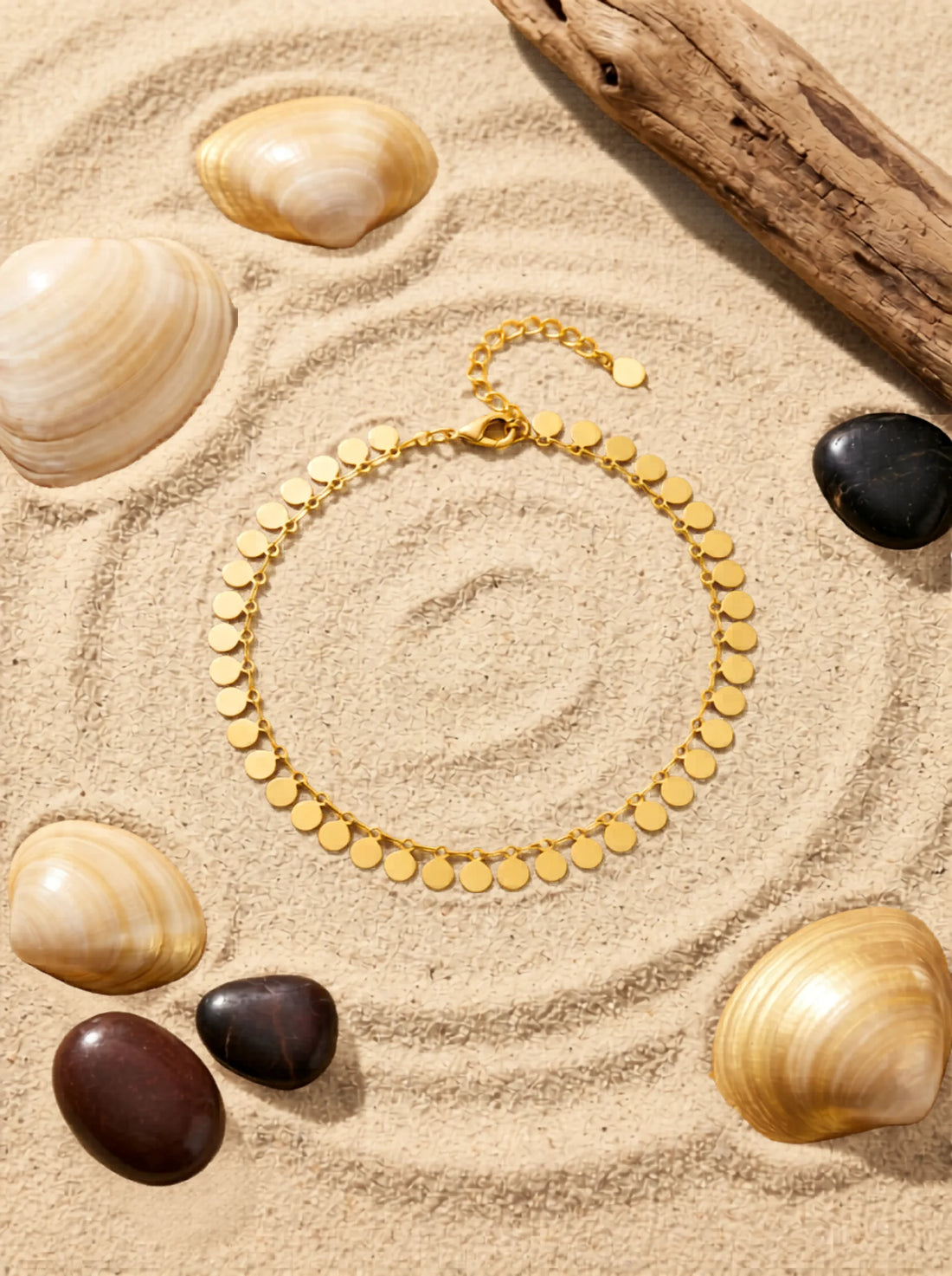 gold plated anklet flat lay on a sandy beach surface.