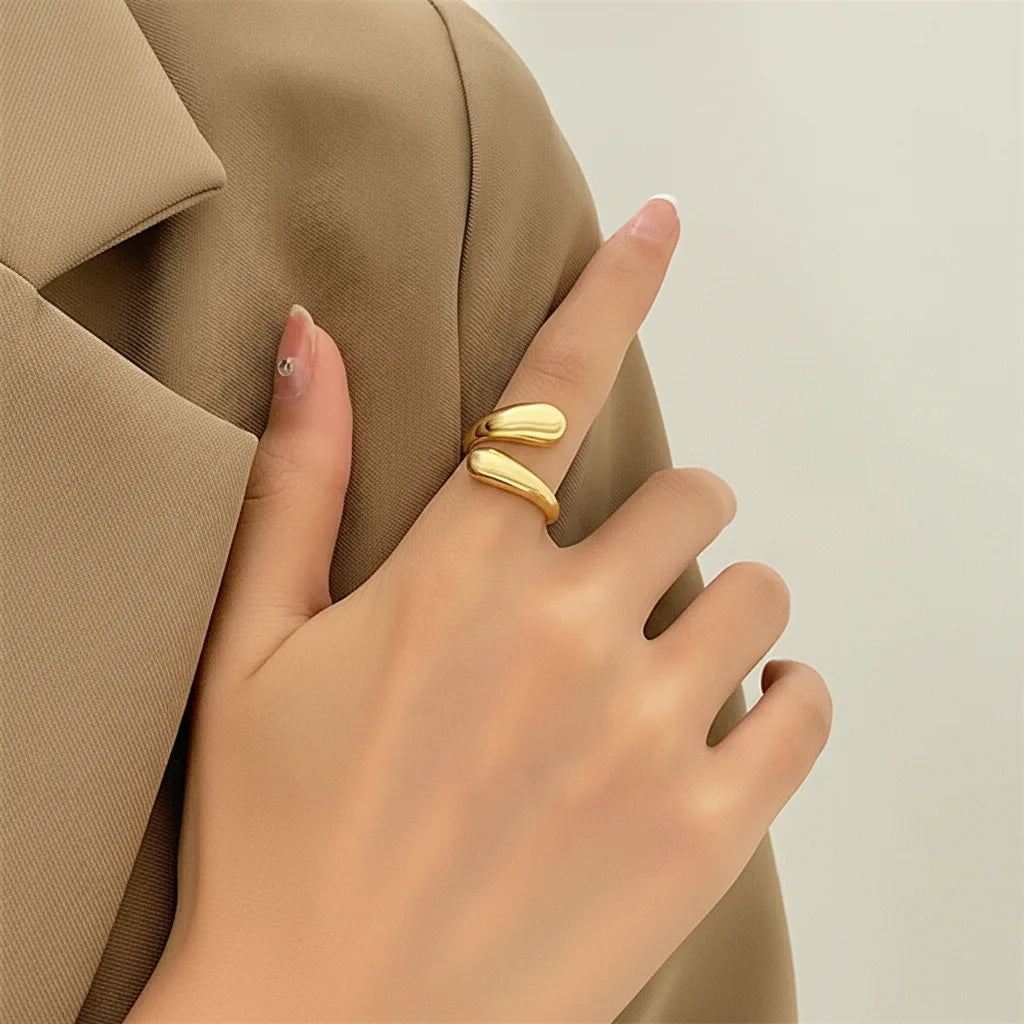 open gold wrap ring close-up on a hand holding a beige blazer lapel, smooth double-wrap ends and clean manicure for chic minimal outfit styling | OriaJewel