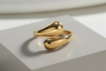 macro product shot of an open gold wrap ring resting on a matte white cube, glossy curved ends and soft natural light creating clean shadows | OriaJewel