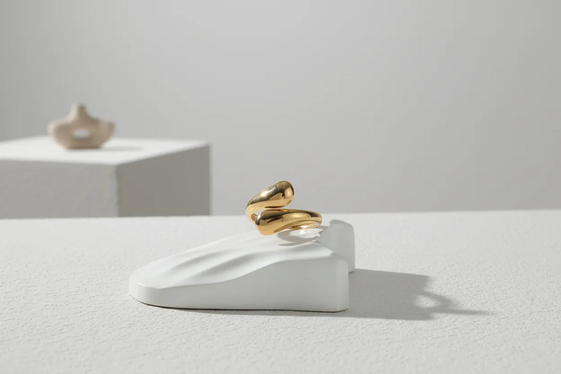 minimal studio scene with an open gold wrap ring balanced on a sculptural white stand, lots of negative space and a crisp shadow for modern styling | OriaJewel