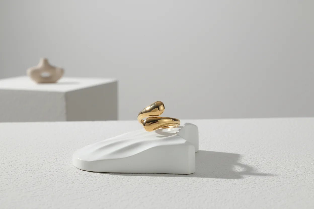 minimal studio scene with an open gold wrap ring balanced on a sculptural white stand, lots of negative space and a crisp shadow for modern styling | OriaJewel