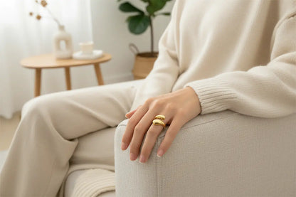 lifestyle shot of an open gold wrap ring worn on a hand resting on a sofa arm, cozy neutral knit outfit and soft daylight for everyday styling | OriaJewel