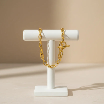 Elegant display of oval link chain bracelet draped over a modern white T-bar jewelry stand against a soft beige backdrop | Oria Jewel