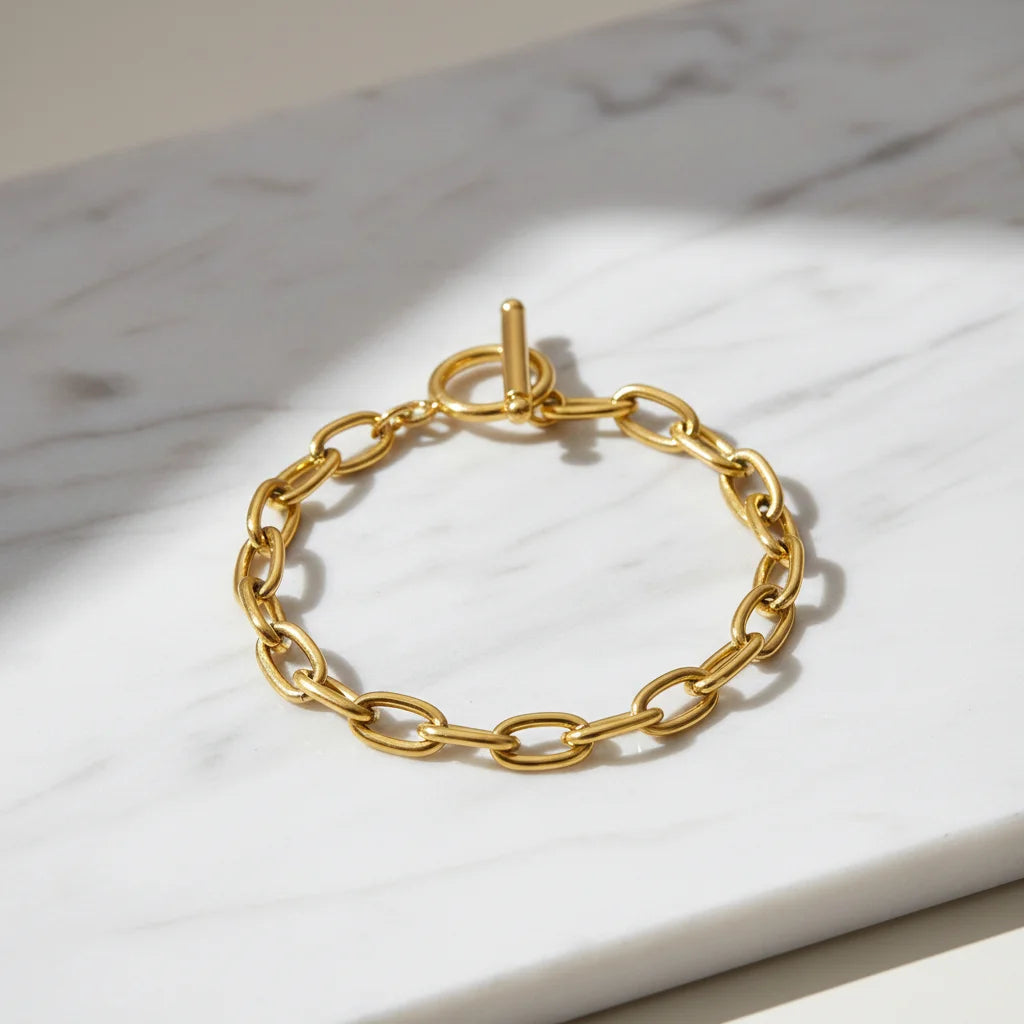 Shiny oval link chain bracelet arranged in a circle on white marble surface with gentle shadows highlighting the bold toggle closure | Oria Jewel