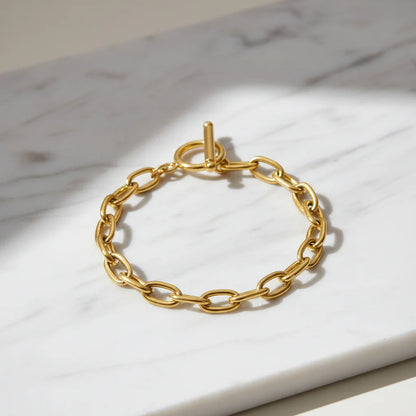Shiny oval link chain bracelet arranged in a circle on white marble surface with gentle shadows highlighting the bold toggle closure | Oria Jewel