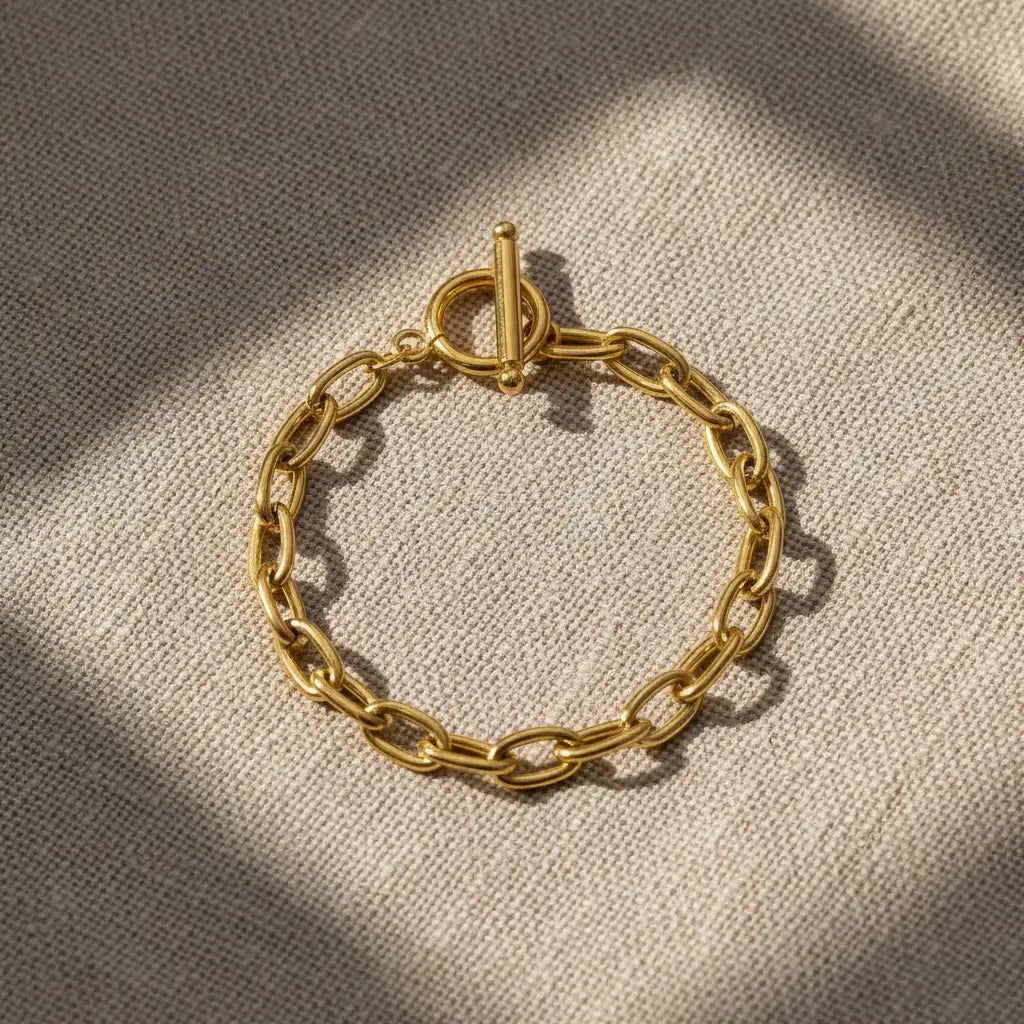 Top view of oval link chain bracelet laid flat on natural linen fabric with windowpane shadows adding a cozy, textured feel | Oria Jewel