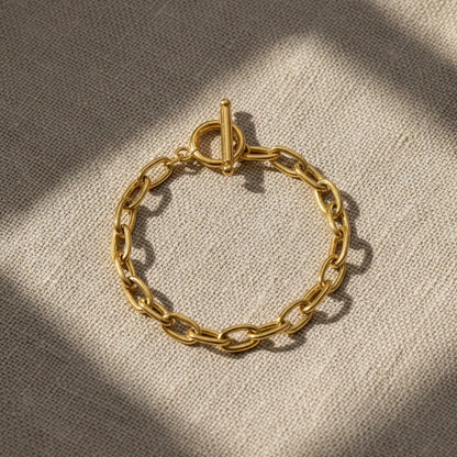 Top view of oval link chain bracelet laid flat on natural linen fabric with windowpane shadows adding a cozy, textured feel | Oria Jewel