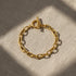 Top view of oval link chain bracelet laid flat on natural linen fabric with windowpane shadows adding a cozy, textured feel | Oria Jewel