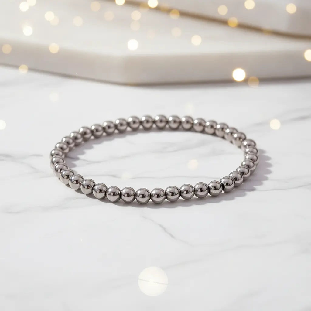 Elegant Silver Beaded Stretch Bracelet made of polished stainless steel beads arranged in a slim circle on a white marble surface with soft glowing bokeh lights in the background | Oria Jewel