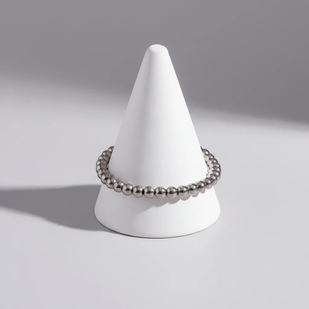 Clean studio product shot of a Silver Beaded Stretch Bracelet displayed around a modern white cone stand, with smooth round beads catching the light against a pale grey background | Oria Jewel