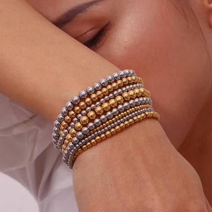 Woman resting her head on her arm while wearing a stack of alternating gold and Silver Beaded Stretch Bracelet strands, showcasing a full layered bracelet look against a soft neutral backdrop | Oria Jewel