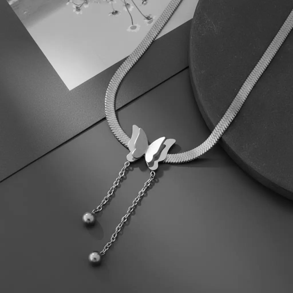 Close-up flat lay of Silver Butterfly Chain Necklace on dark surface showing double butterfly detail and long chain drops | Oria Jewel