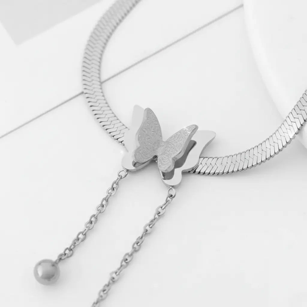 Macro shot of pendant section of Silver Butterfly Chain Necklace highlighting textured butterfly wings and smooth chain tassels | Oria Jewel