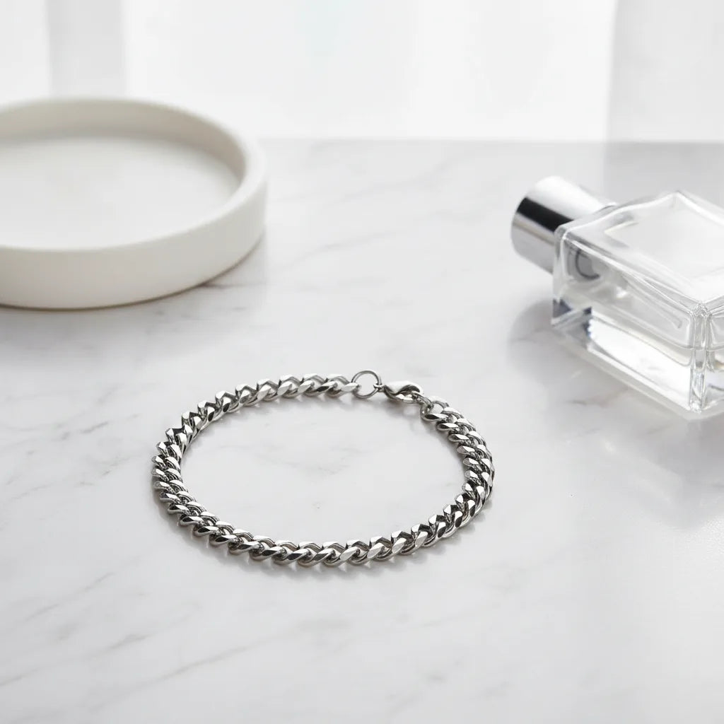 Elegant silver chain bracelet displayed in a circle on a white marble surface, styled with a minimal round dish and a clear glass perfume bottle for a clean, modern look | Oria Jewel
