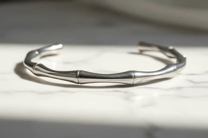 Close-up of a bamboo-textured silver cuff bracelet resting on a white marble surface, its smooth segmented design catching soft natural light | Oria Jewel