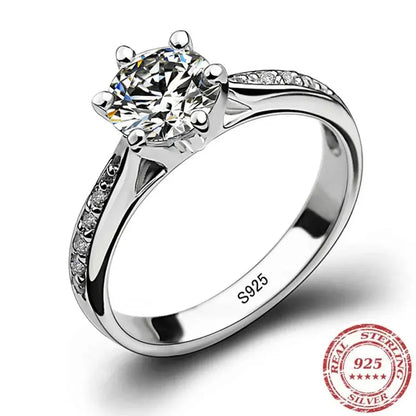 Studio white-background product shot of a silver cz solitaire ring featuring a round CZ in a prong setting, pavé accents on the shoulders, visible S925 engraving, and a 925 sterling silver seal graphic | OriaJewel