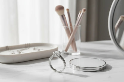 Bright vanity countertop setup showing a silver cz solitaire ring standing near makeup brushes, a compact mirror, and a jewelry tray on a clean marble surface in soft daylight | OriaJewel