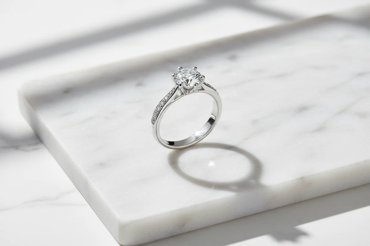 Clean marble flat-lay featuring a silver cz solitaire ring standing upright with crisp natural light, a defined shadow ring, and a bright sparkle on the round CZ stone | OriaJewel