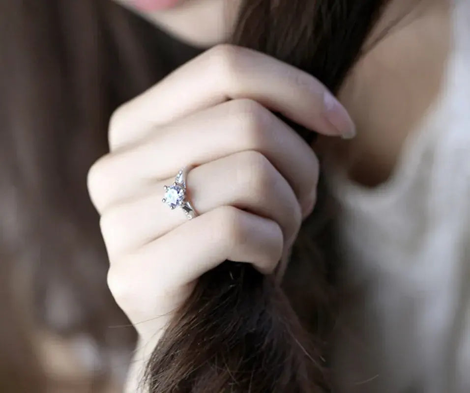 Lifestyle close-up of a woman’s hand wearing a silver cz solitaire ring while holding her hair, with the round CZ stone and pavé band details in sharp focus against a soft blurred background | OriaJewel