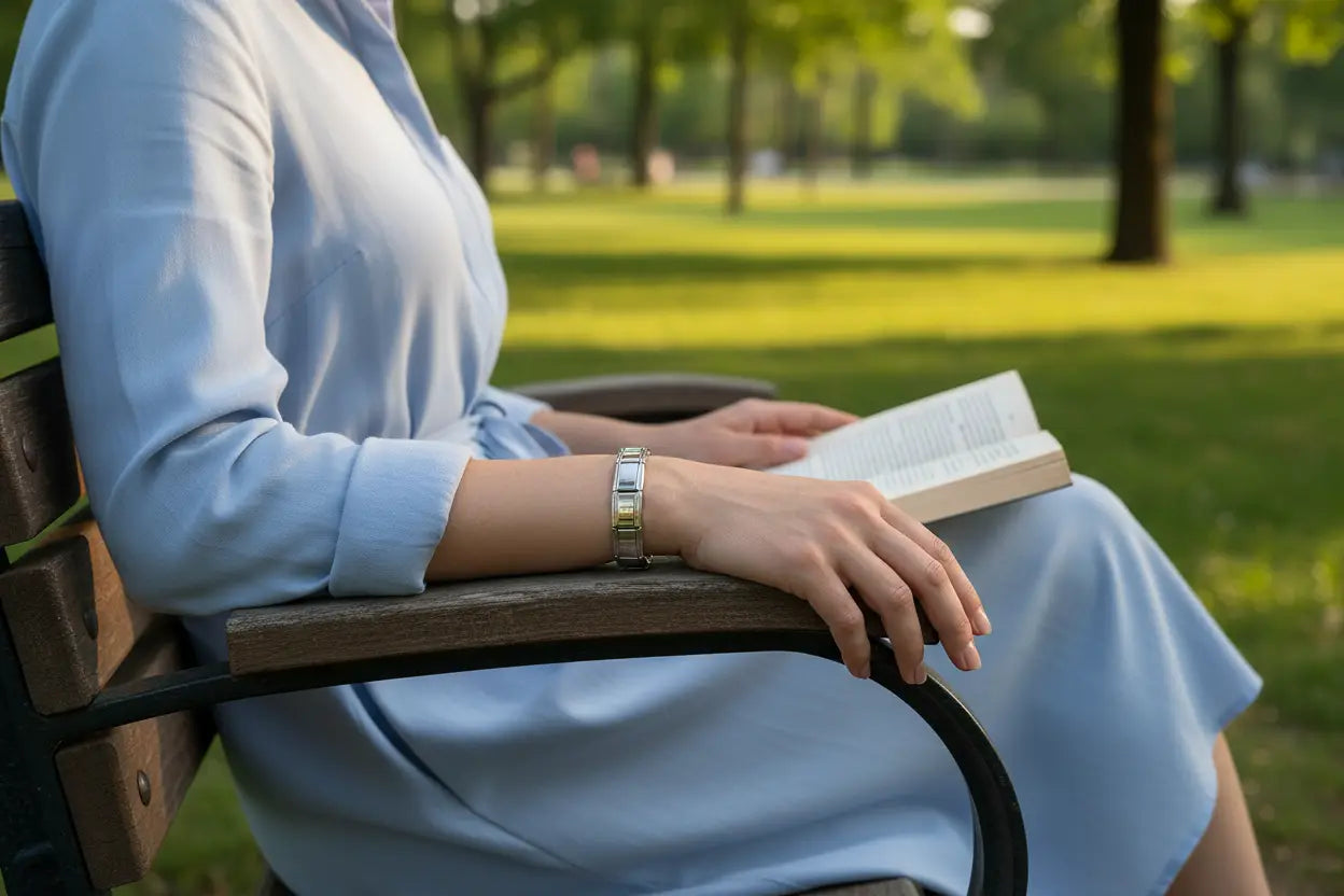 Relaxed woman sitting on a park bench reading a book, wearing a chic silver stainless steel stretch bracelets bracelets that stands out against her light blue dress in the soft afternoon sunlight | Oria Jewel