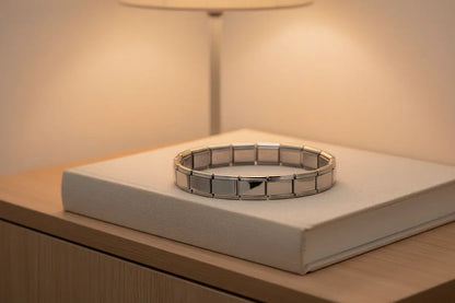 Cozy nightstand scene featuring a glowing lamp and a closed fabric-covered book, with a silver stainless steel stretch bracelets bracelets neatly resting on top, highlighting its clean, modern look for everyday wear | Oria Jewel