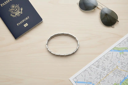 Travel-inspired flat lay with a passport, aviator sunglasses, and a city map arranged around a circular silver stainless steel stretch bracelets bracelets, suggesting a stylish companion for on-the-go adventures | Oria Jewel