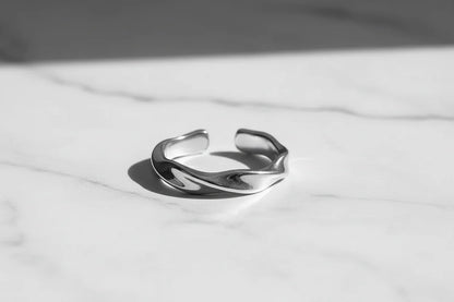 Macro close-up of a silver wave ring on white marble surface, highlighting the open adjustable band and smooth sculpted wave twist with crisp shadow | OriaJewel