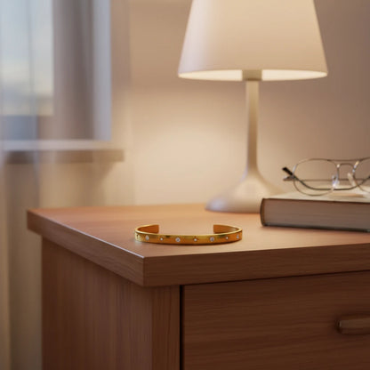 Gold star cuff bracelet resting on a wooden bedside table beside a lamp, book and glasses, styled as a favorite nightstand accessory ready for everyday wear | Oria Jewel
