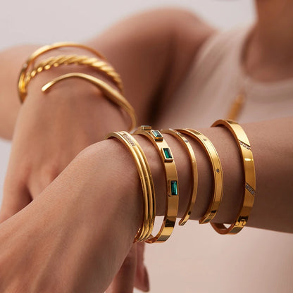 Close-up of stacked gold bangles on both wrists, with a polished statement cuff bracelet in the center of the arm stack creating a bold, glamorous look | Oria Jewel