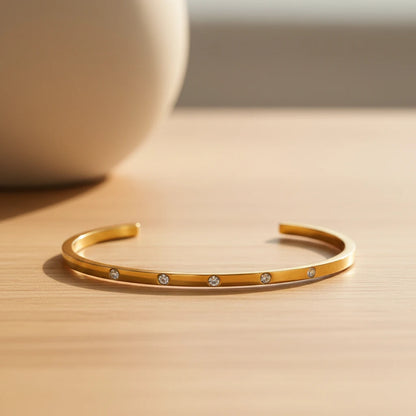 Minimalist scene with a thin gold cuff bracelet resting open on a light wooden surface in soft daylight, highlighting its slim profile and evenly spaced crystal accents | Oria Jewel